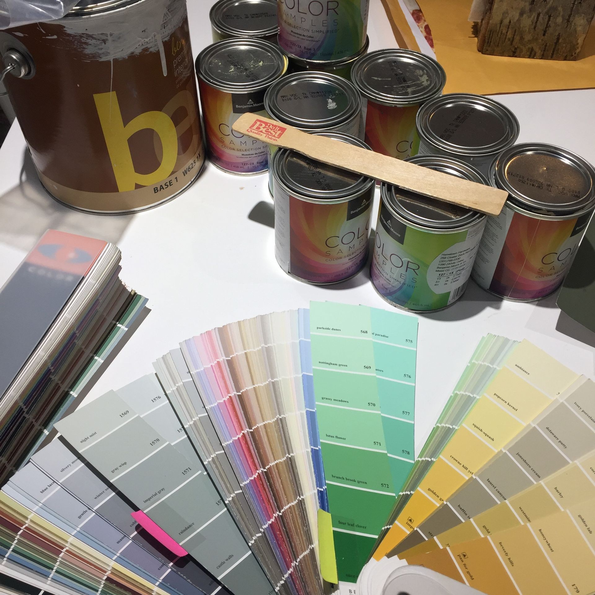 Assorted paint cans and color swatches on a table, with a wooden paint stirrer.