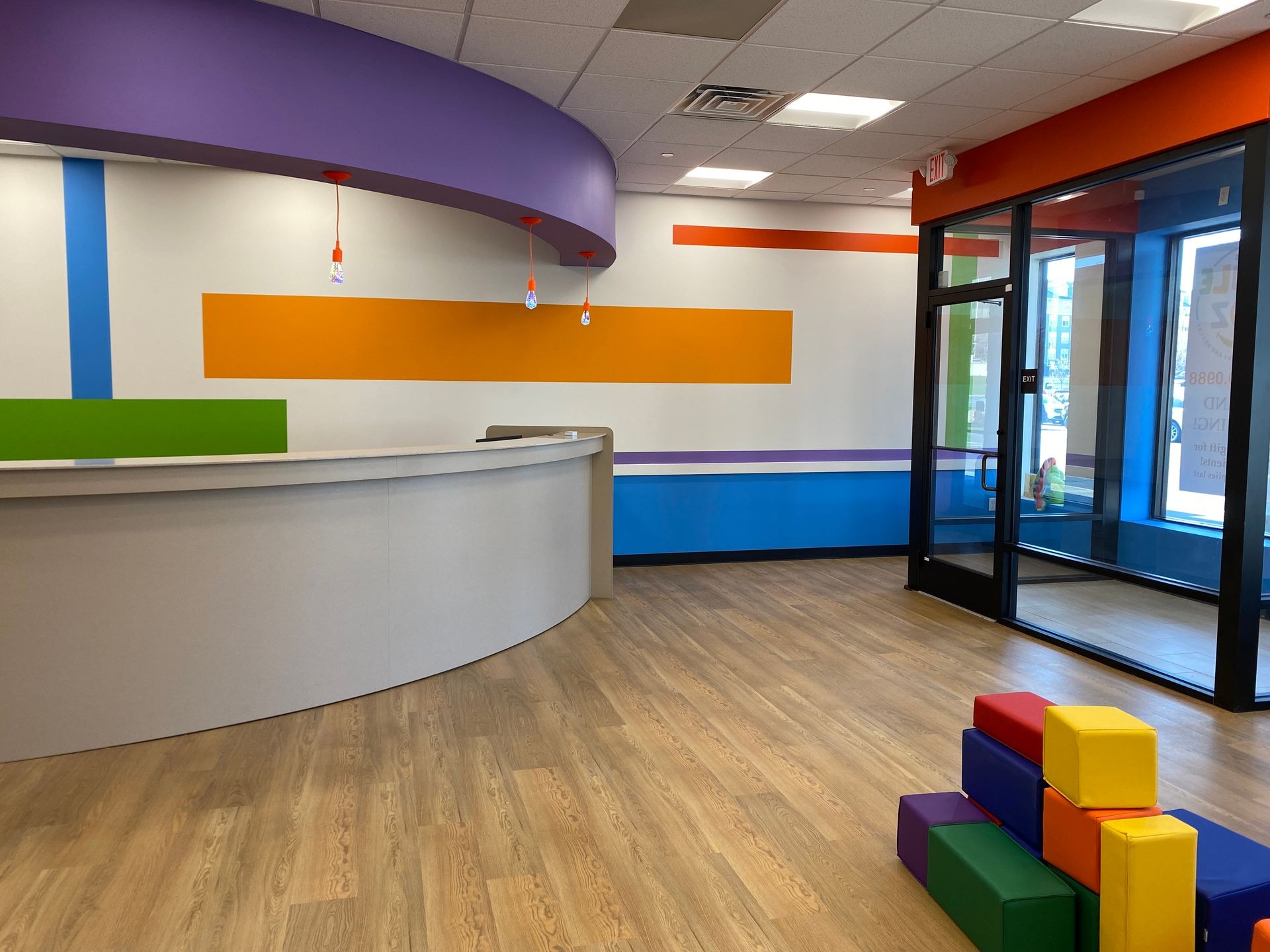 Colorful waiting area in pediatric dentist office with curved desk and stack of bright foam blocks on wooden floor.